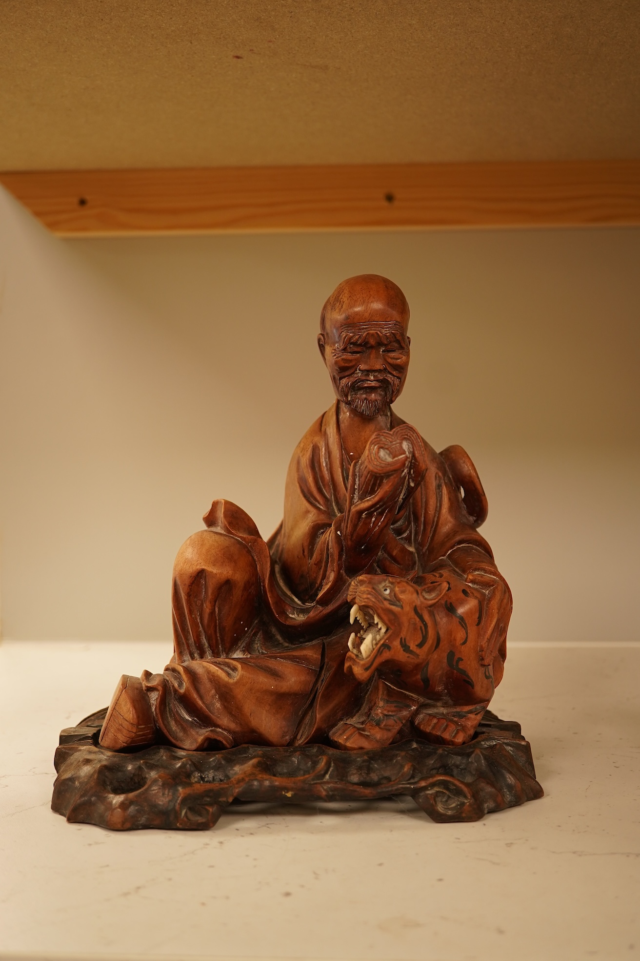 A Chinese hardwood carving of a seated luohan and tiger on hardwood stand, 24cm high including stand.